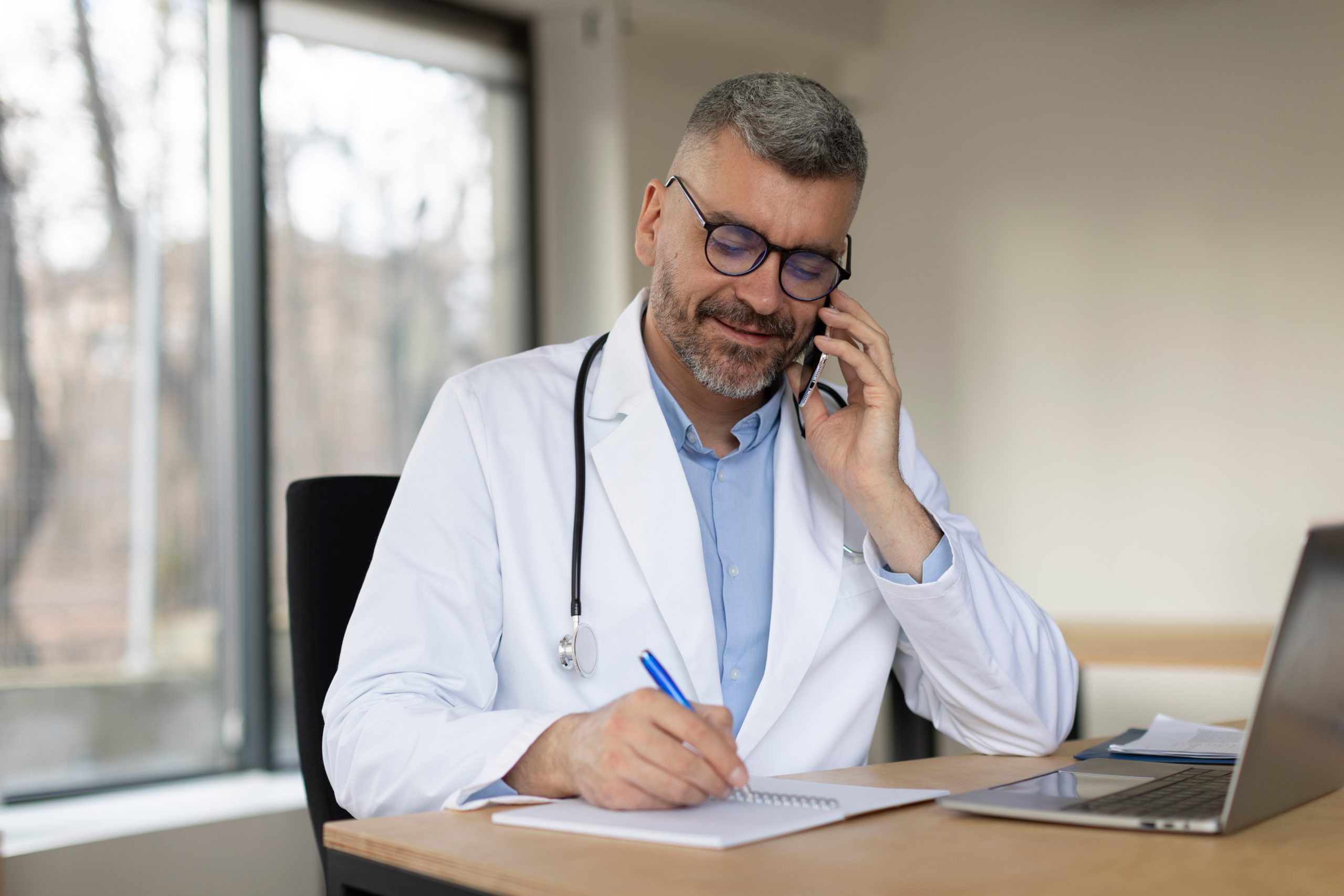 Smiling european middle aged male doctor talking on phone at work